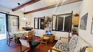 A cozy living room with a wooden ceiling, a dining table with chairs, a sofa, and a television on a wooden side table. - Trilocale in Centro con Giardino (San Teodoro)