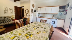 A compact kitchen with basic appliances, a dining area with a table set for two, and a cozy living space with a sofa and a chair. - Trilocale in Centro con Giardino (San Teodoro)