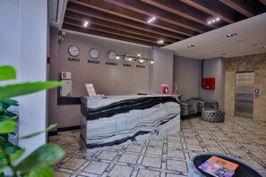 A reception area with a marble counter, clocks displaying different cities, and a seating area with ottomans.