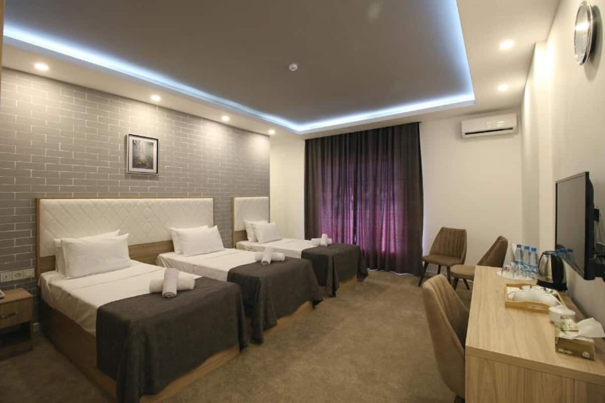 A hotel room with two beds, a desk, a chair, a TV, and an air conditioning unit.