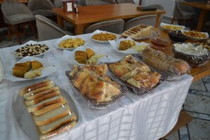 A buffet table with various food items, including bread, pastries, and desserts, covered with plastic wrap.
