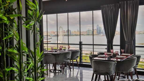 A dining area with tables and chairs, large windows with a view of a city skyline and a body of water. - ZAM-ZAM (Baku)