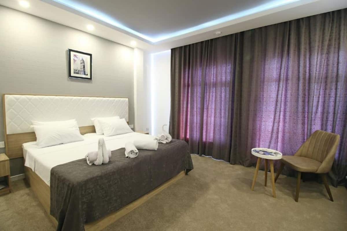 A hotel room with a bed, a chair, a small table, and a window with curtains.