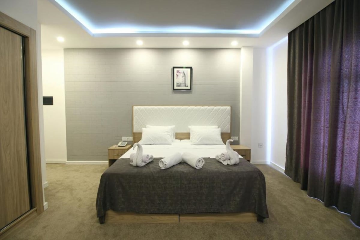 Une chambre d’hôtel moderne avec un grand lit, une table de chevet, un tableau encadré au mur et un rideau à la fenêtre.