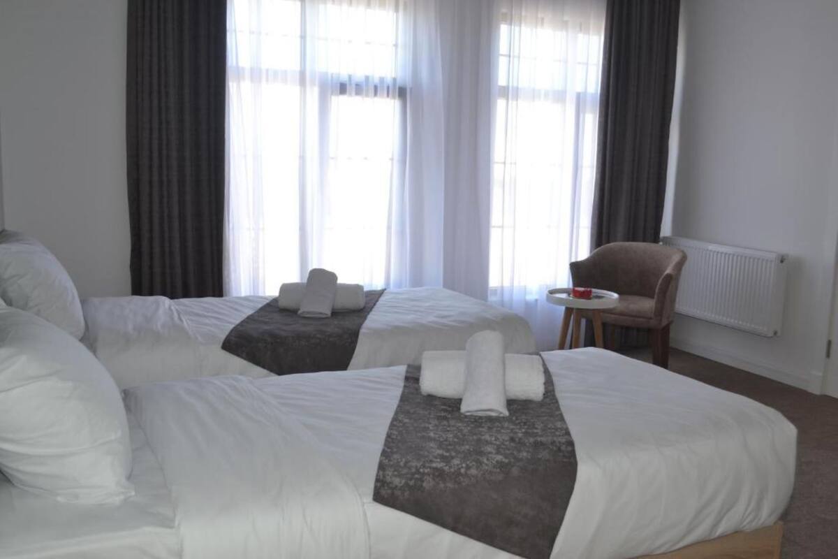 A hotel room with two beds, a small table, a chair, and a window with curtains.