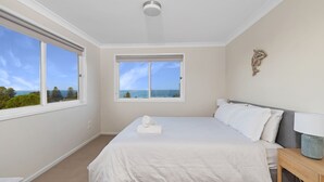 Ein Schlafzimmer mit einem großen Bett, zwei Fenstern mit Meerblick, einer Deckenleuchte und einem an der Wand befestigten Dekorationsgegenstand.