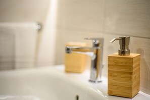 A bathroom with a wooden soap dispenser on a sink, a mirror, and a towel hanging on a rack.