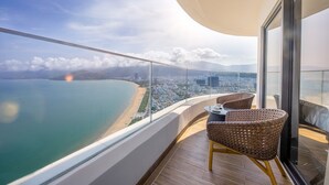Un balcón con sillas de mimbre, una mesa y vistas a la playa y al paisaje urbano.