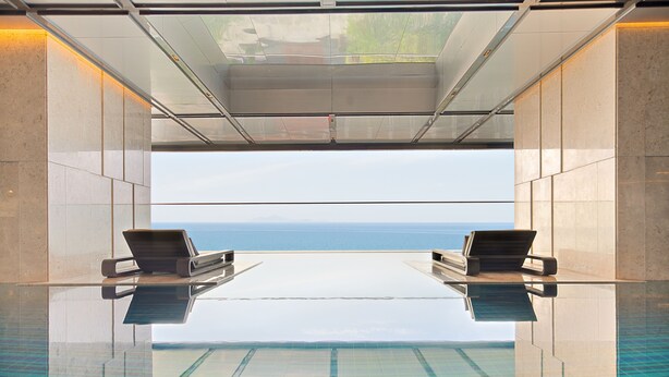 Una piscina infinita con dos sillas de descanso frente a una vista despejada del mar.