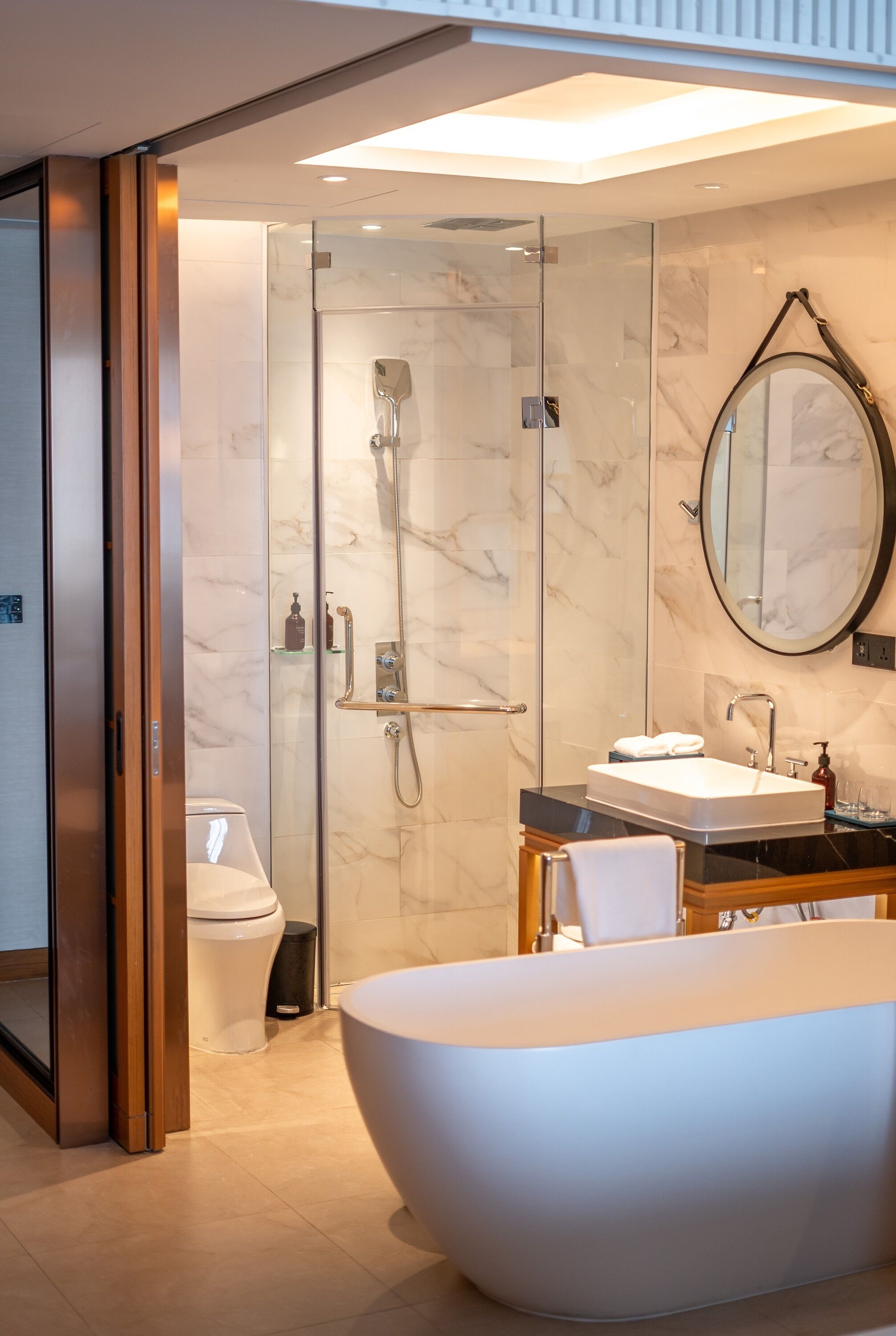A modern bathroom with a glass-enclosed shower, a freestanding bathtub, a vanity with a sink, and a large mirror.