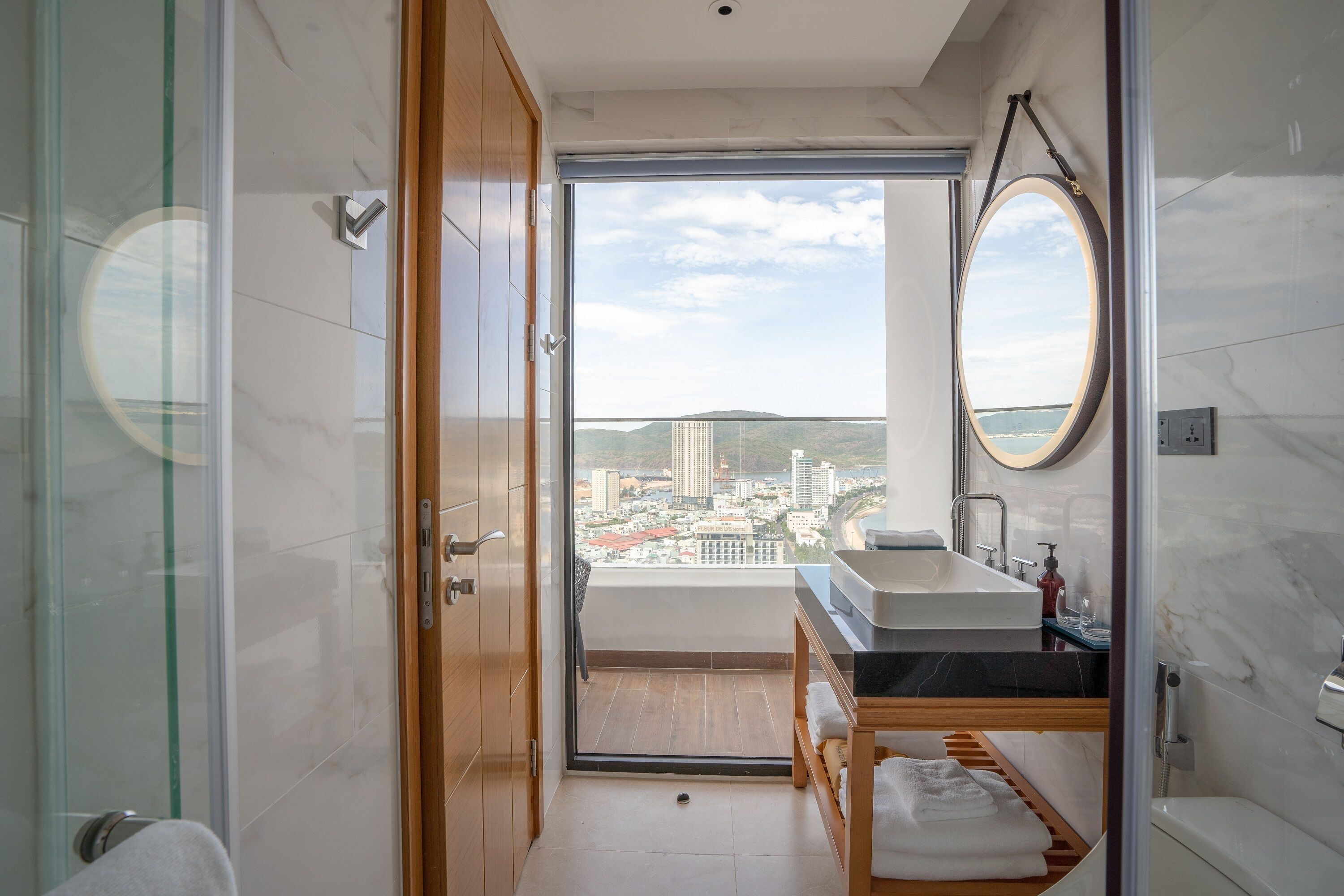 Een moderne badkamer met uitzicht op een balkon, een grote spiegel en een houten bankje.