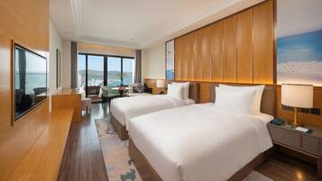 A hotel room with two beds, a desk, a chair, a view of the city, and a large window.