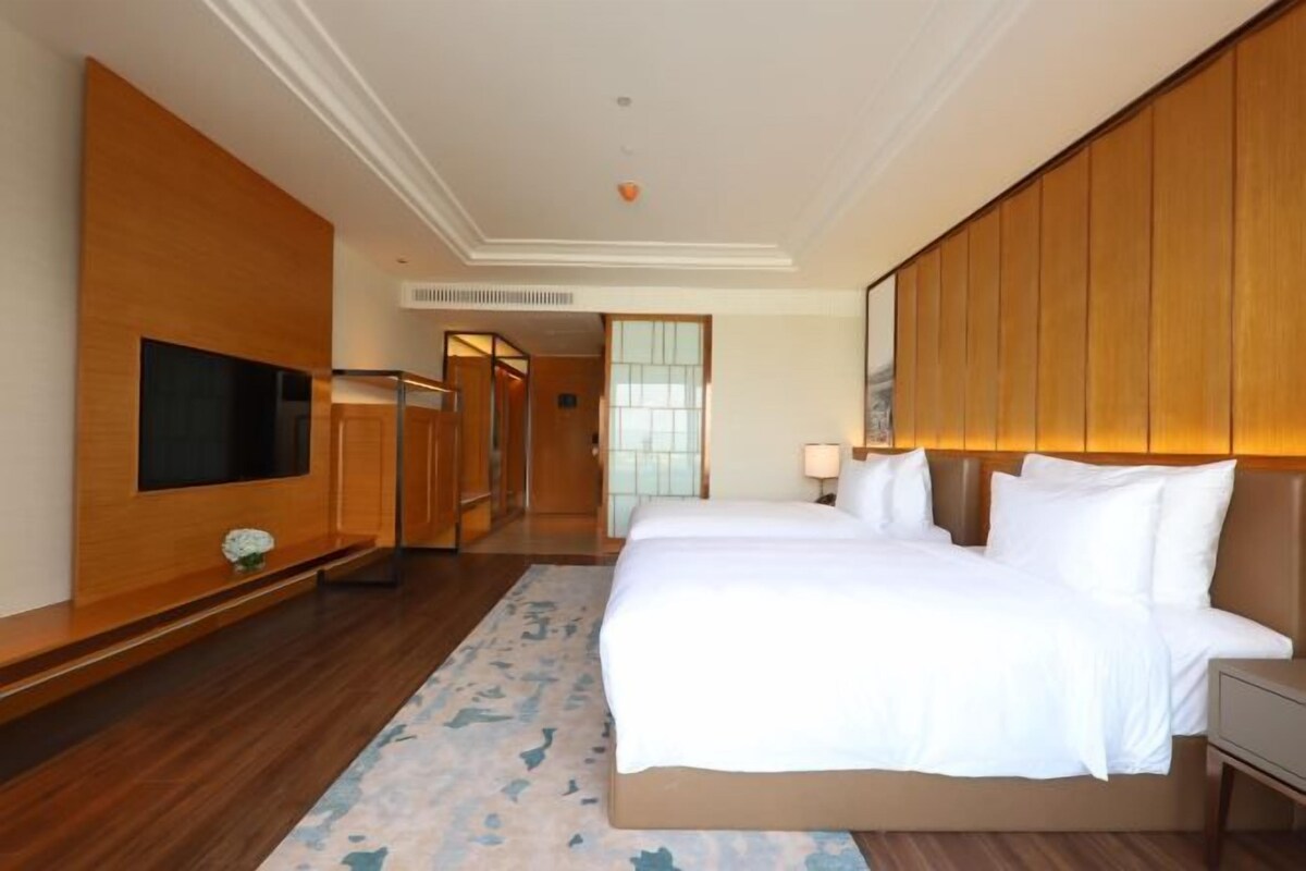 A hotel room with a large bed, wooden paneling, a flat-screen TV, and a view of the hallway.