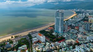Un paisaje urbano costero con un hotel alto y llamativo, una playa y edificios residenciales aledaños.