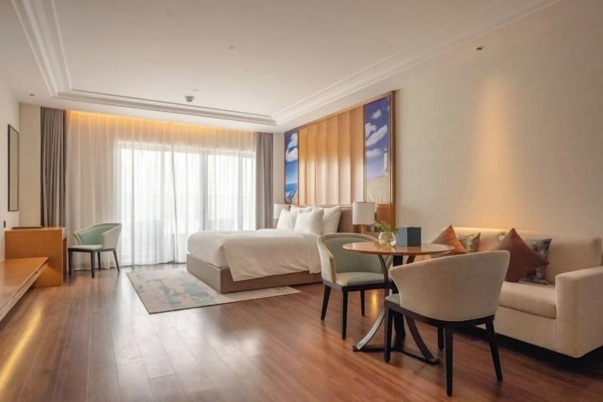 A hotel room with a large bed, two armchairs, a small round table, and a sofa.