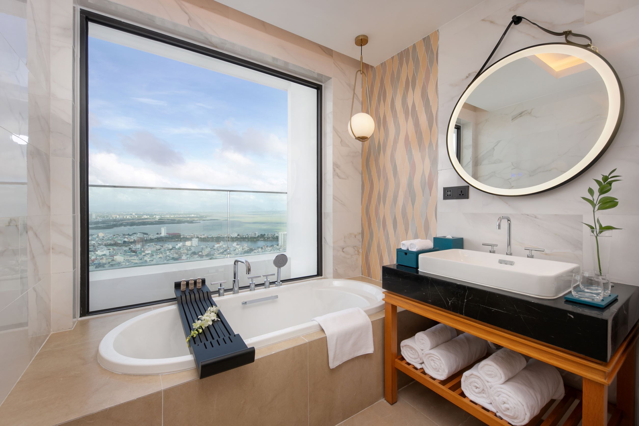 Une salle de bain moderne avec une grande baignoire, un meuble-lavabo avec un évier, un miroir et une vue sur le paysage urbain par une grande fenêtre.