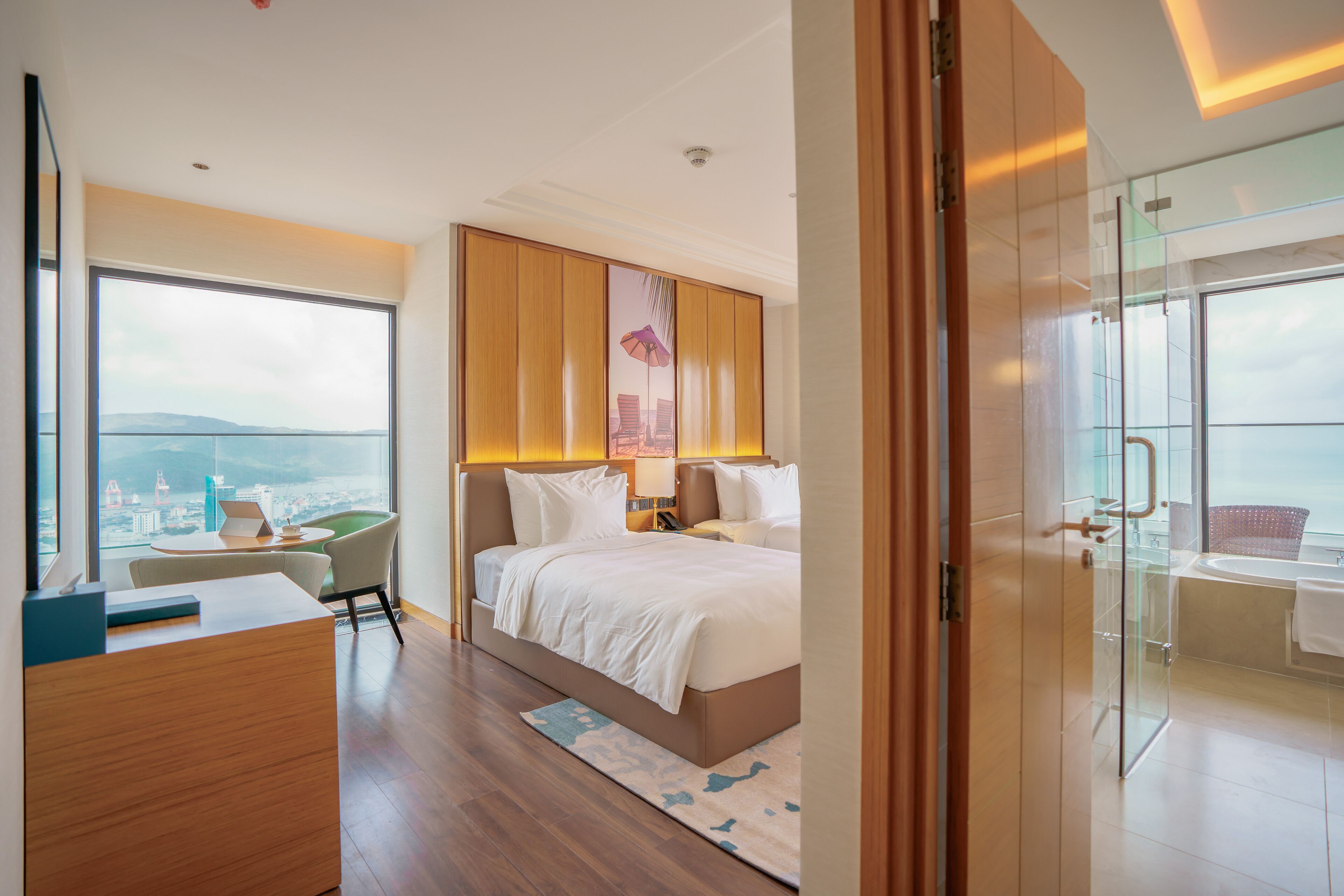 A modern hotel room with a large bed, a desk, a chair, and a view of the city.