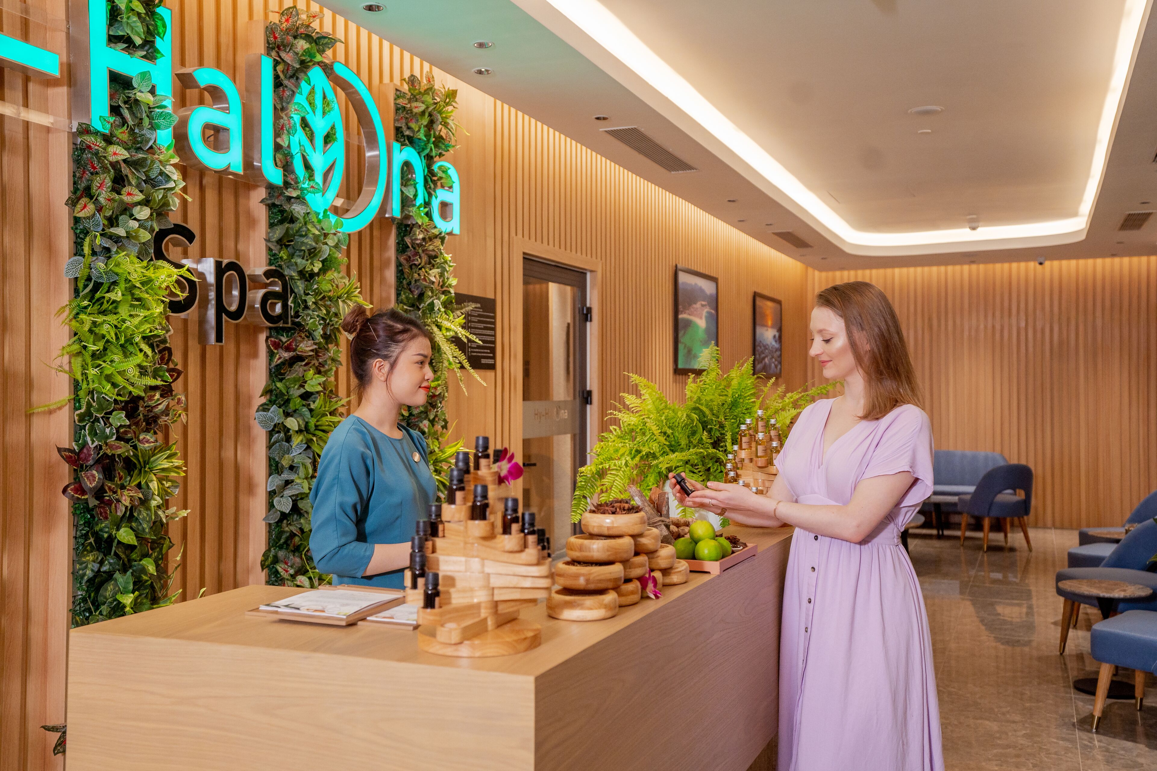 A reception desk with a wooden finish, a neon sign reading "Hana Spa", and a wall decorated with plants.