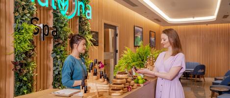 A reception desk with a wooden finish, a neon sign reading "Hana Spa", and a wall decorated with plants.