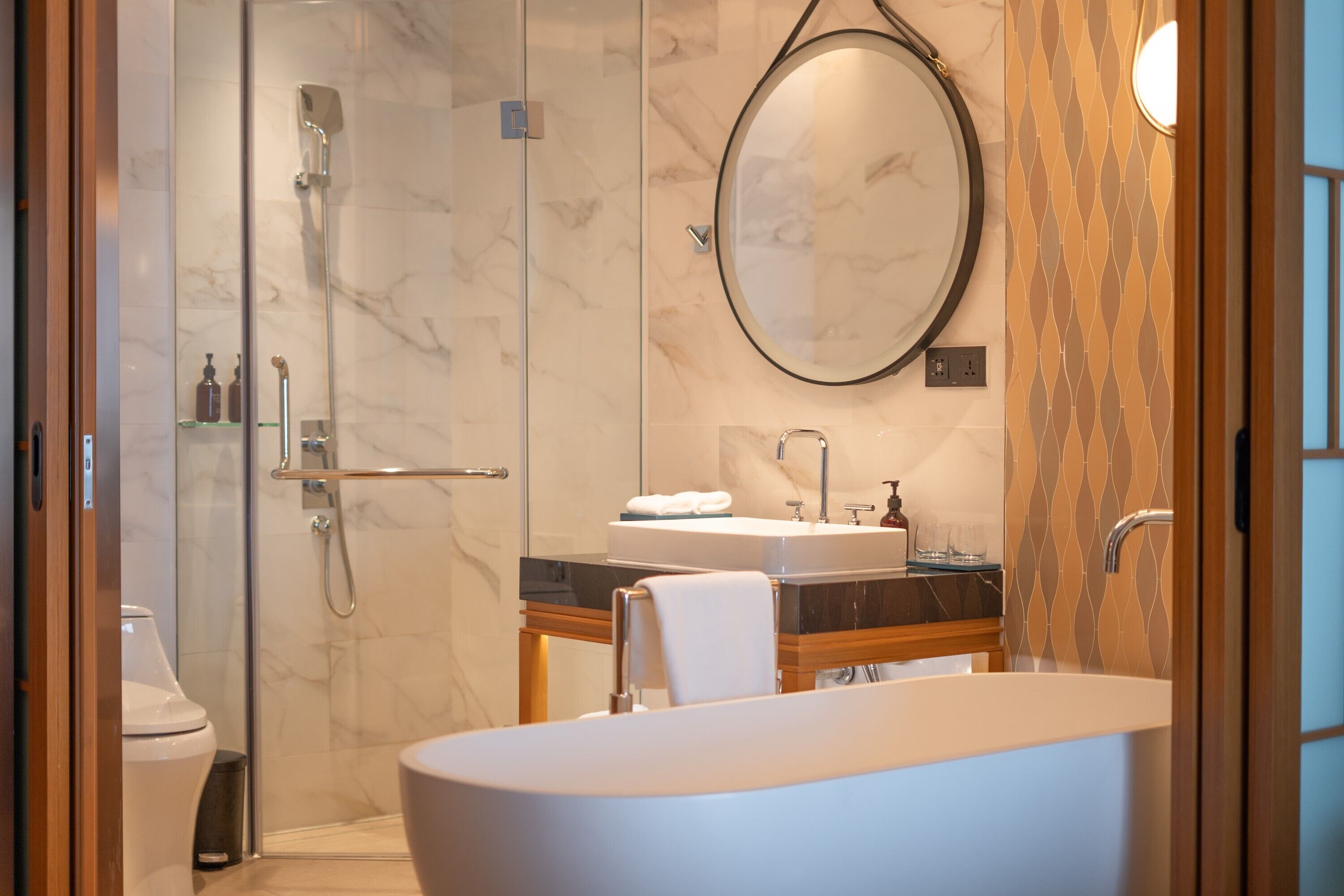 A modern bathroom with a glass-enclosed shower, a large oval mirror, a freestanding bathtub, and a vanity with a sink and countertop.
