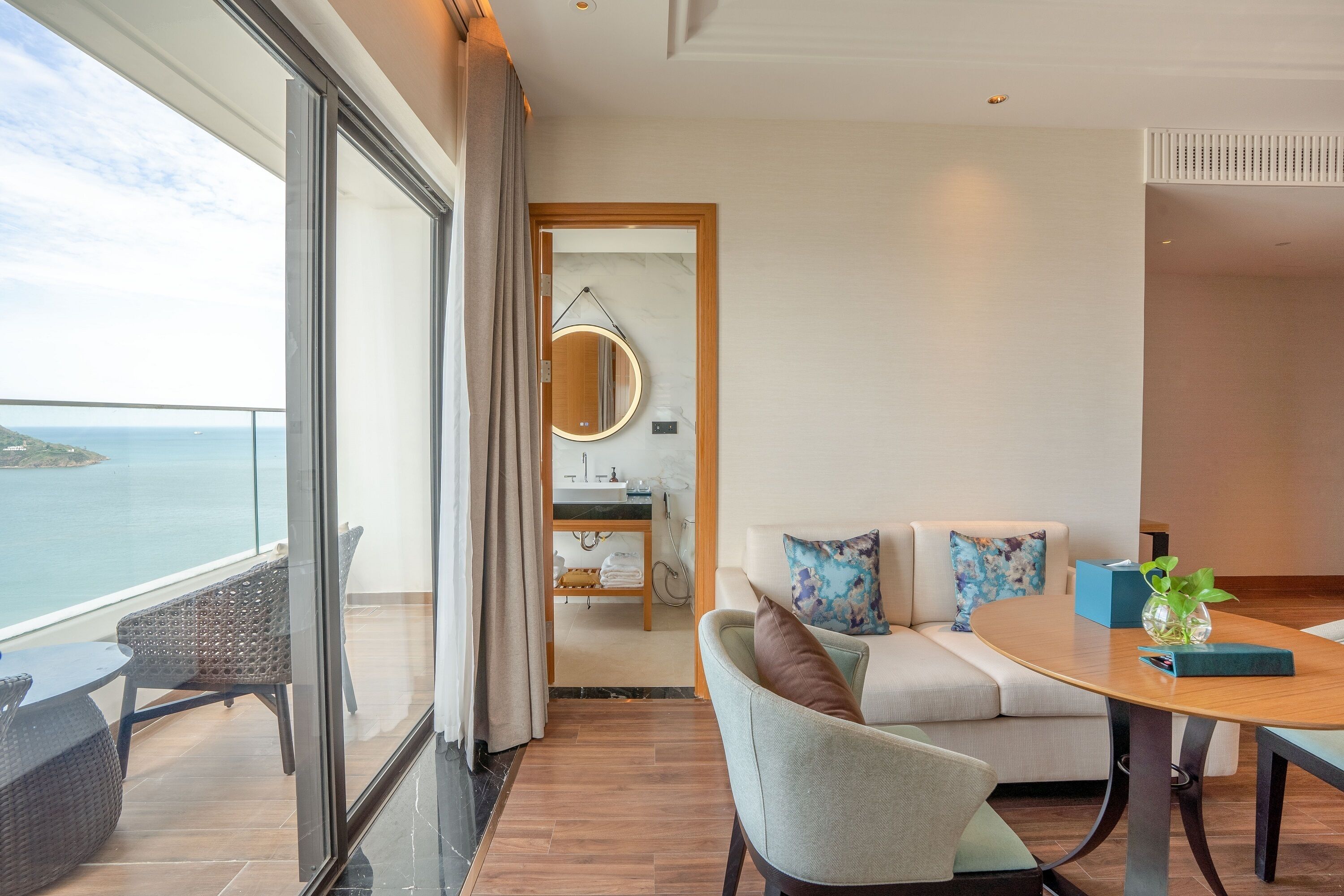 A modern hotel room with a balcony, a round table, a sofa, and a view of the sea.