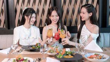 Three people seated at a table with various dishes and drinks, in a room with a geometric patterned wall.