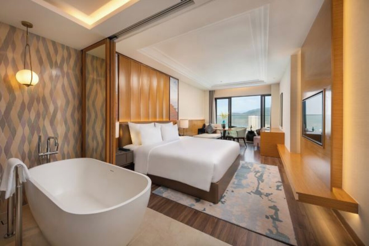 A modern hotel room with a large bed, a bathtub, and a view of the sea.