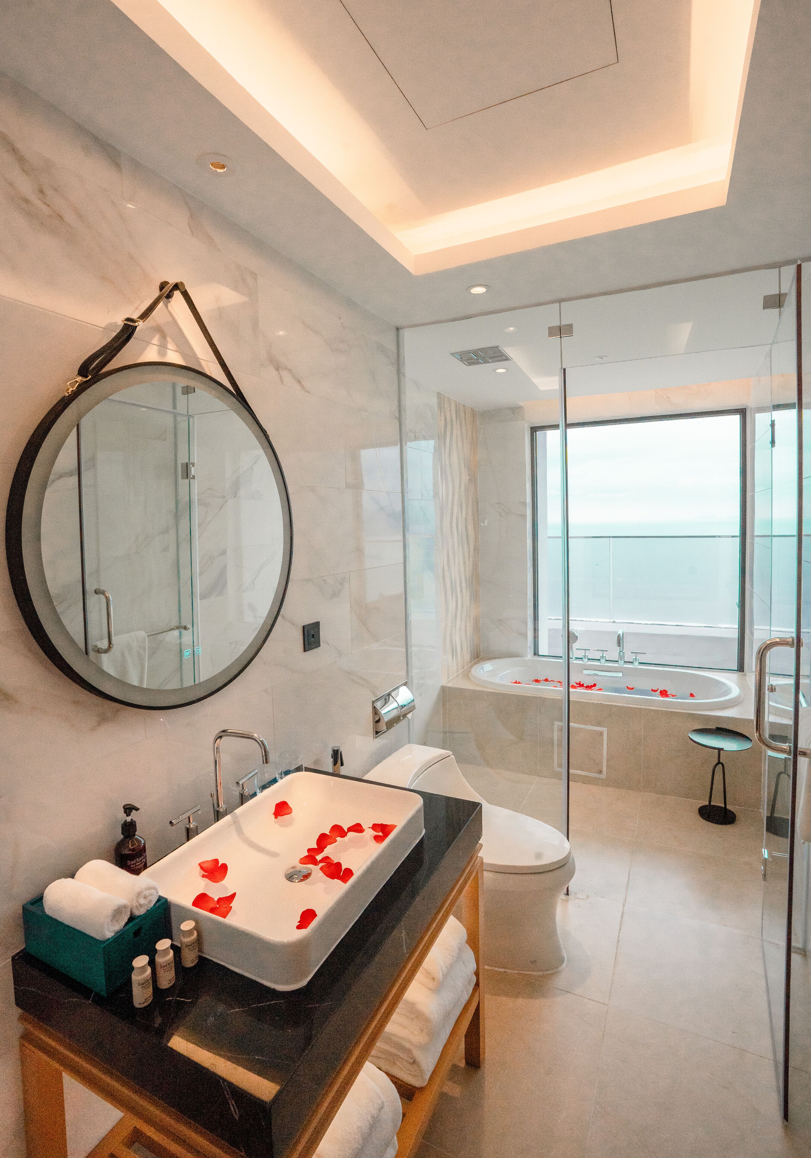 Une salle de bain moderne avec un grand miroir, une baignoire et un lavabo décoré de pétales de rose.