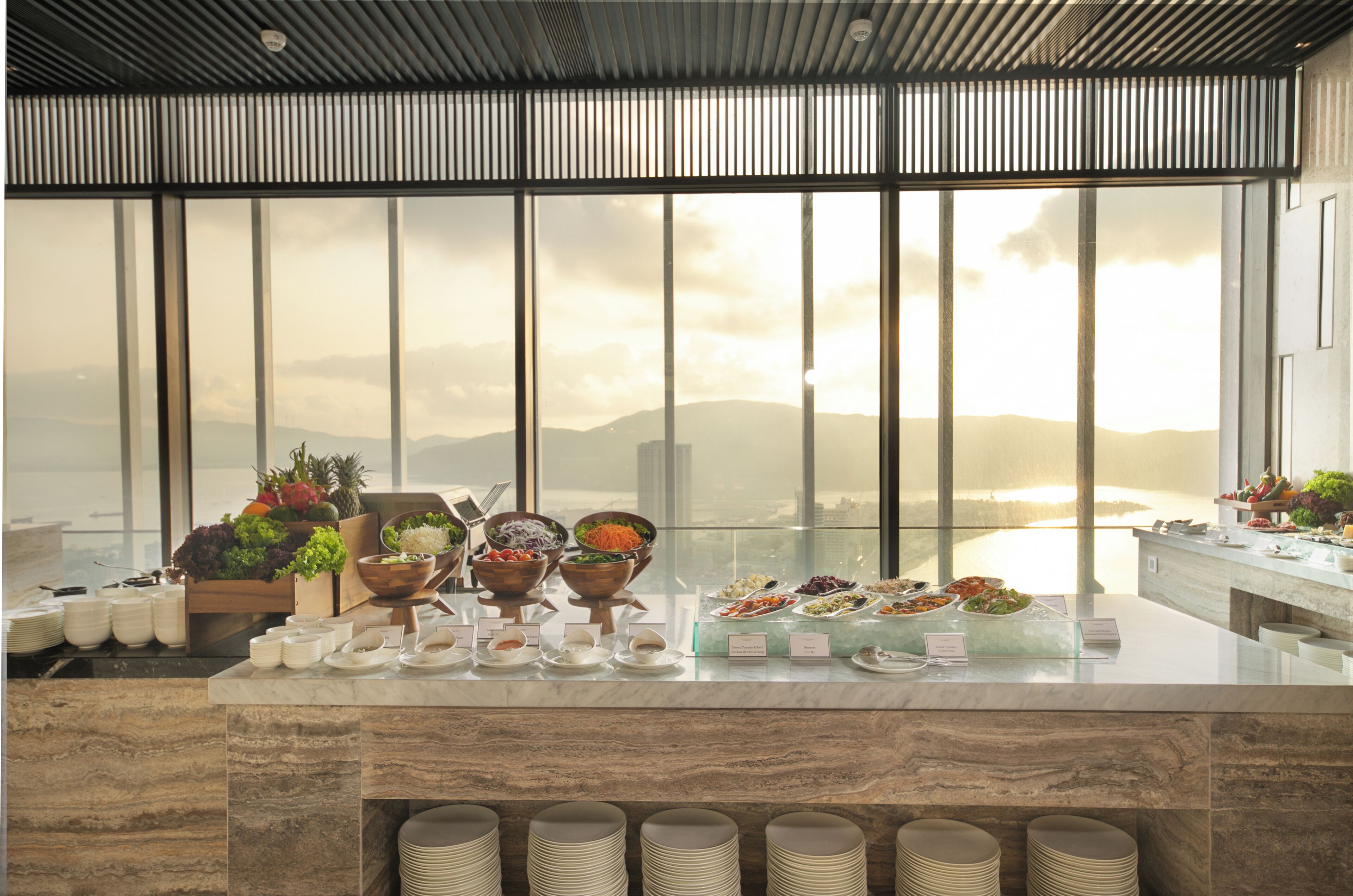 A buffet setup with various food items and a view of a mountainous landscape through large windows.