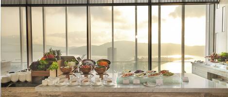 A buffet setup with various food items and a view of a mountainous landscape through large windows.