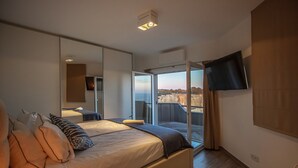 A modern bedroom with a large bed, a TV mounted on the wall, and a balcony with a city view. - Oceanfront Villa with three bedrooms plus one (Lagoa)