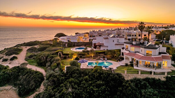 A coastal resort with multiple buildings, a swimming pool, and a view of the ocean at sunset. - Oceanfront Villa with three bedrooms plus one (Lagoa)