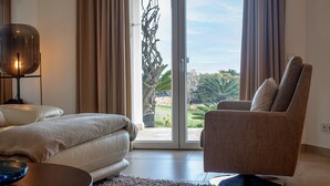 A modern bedroom with a sofa, a bed, and a view of a garden through a sliding glass door. - Oceanfront Villa with three bedrooms plus one (Lagoa)