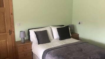 A bedroom with a bed, a nightstand, a wooden door, and a light green wall.