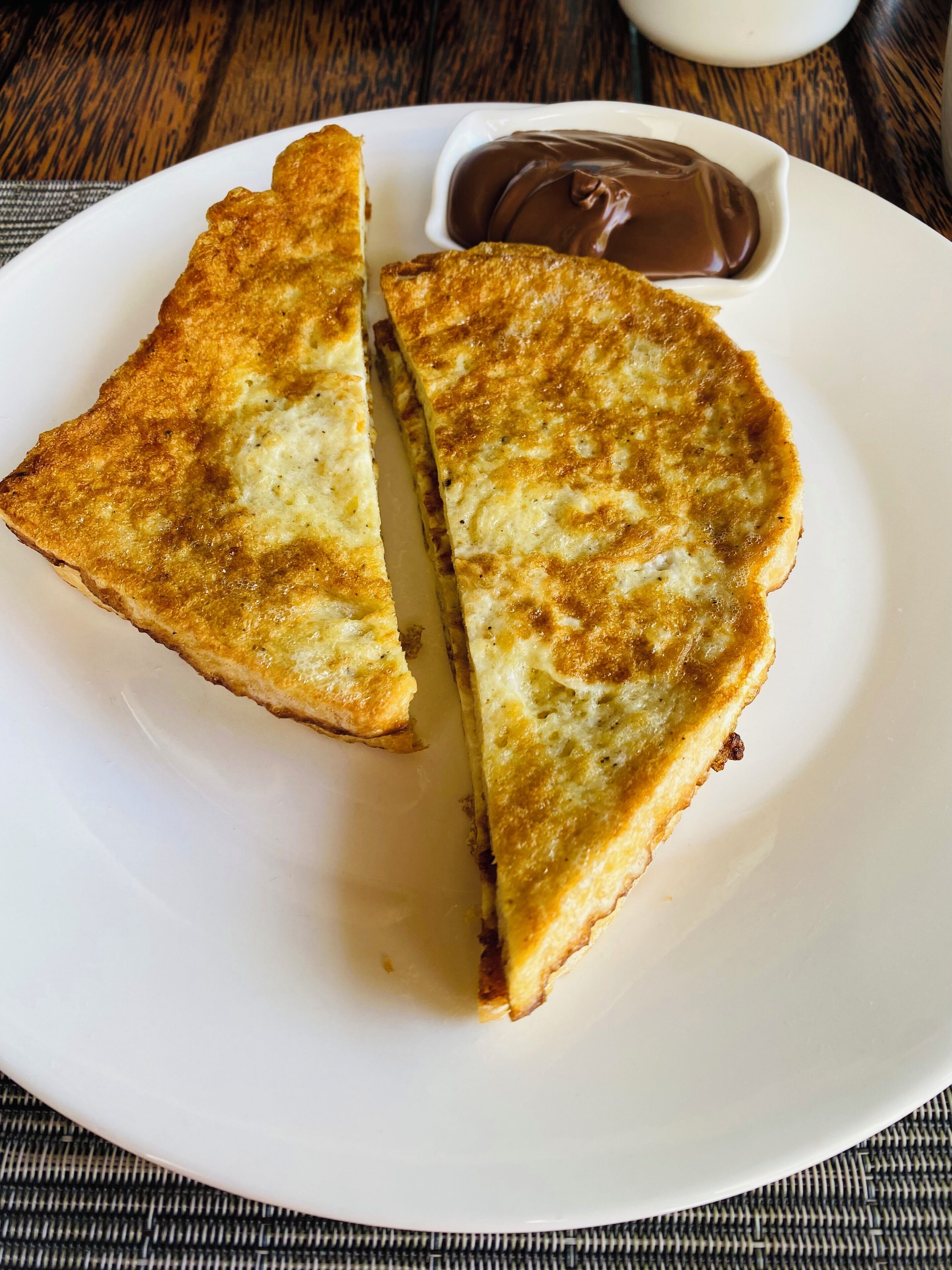 A plate with a triangular food item and a small bowl of chocolate sauce.