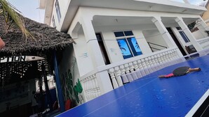 A multi-story building with a blue pool table and a thatched-roof structure nearby. - Nungwi Beach Front (Nungwi)