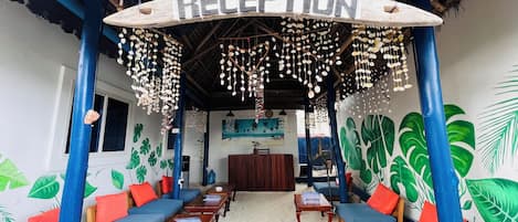 Un área de recepción con techo de paja, muebles de madera y un mural en la pared.