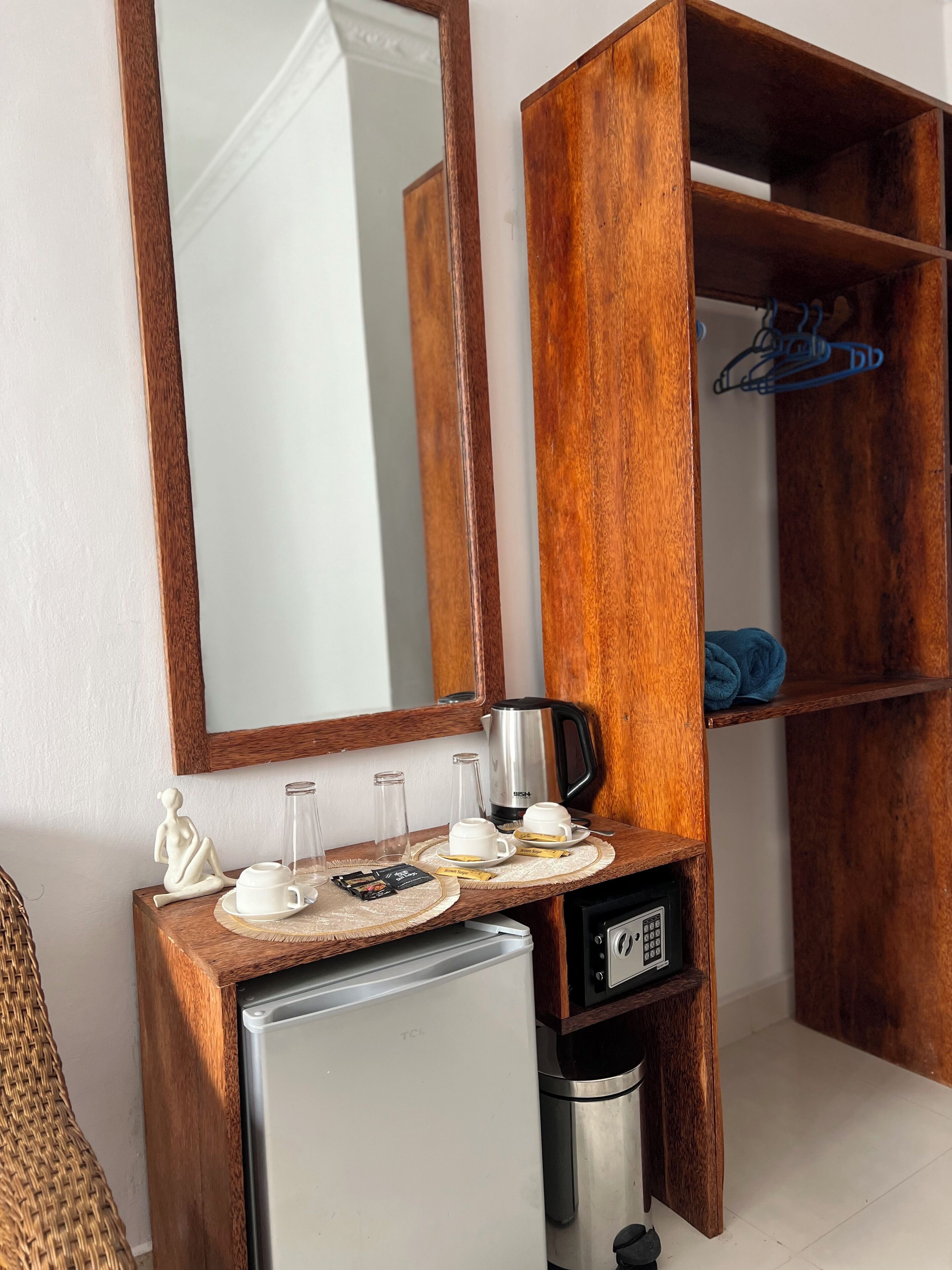A compact kitchenette with a refrigerator, coffee maker, and a wooden shelf with a folded towel.