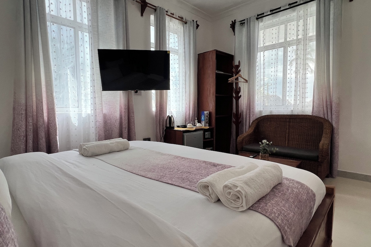 Habitació d'hotel amb llit, televisió, armari de fusta, cadira i escriptori amb tetera i tasses.