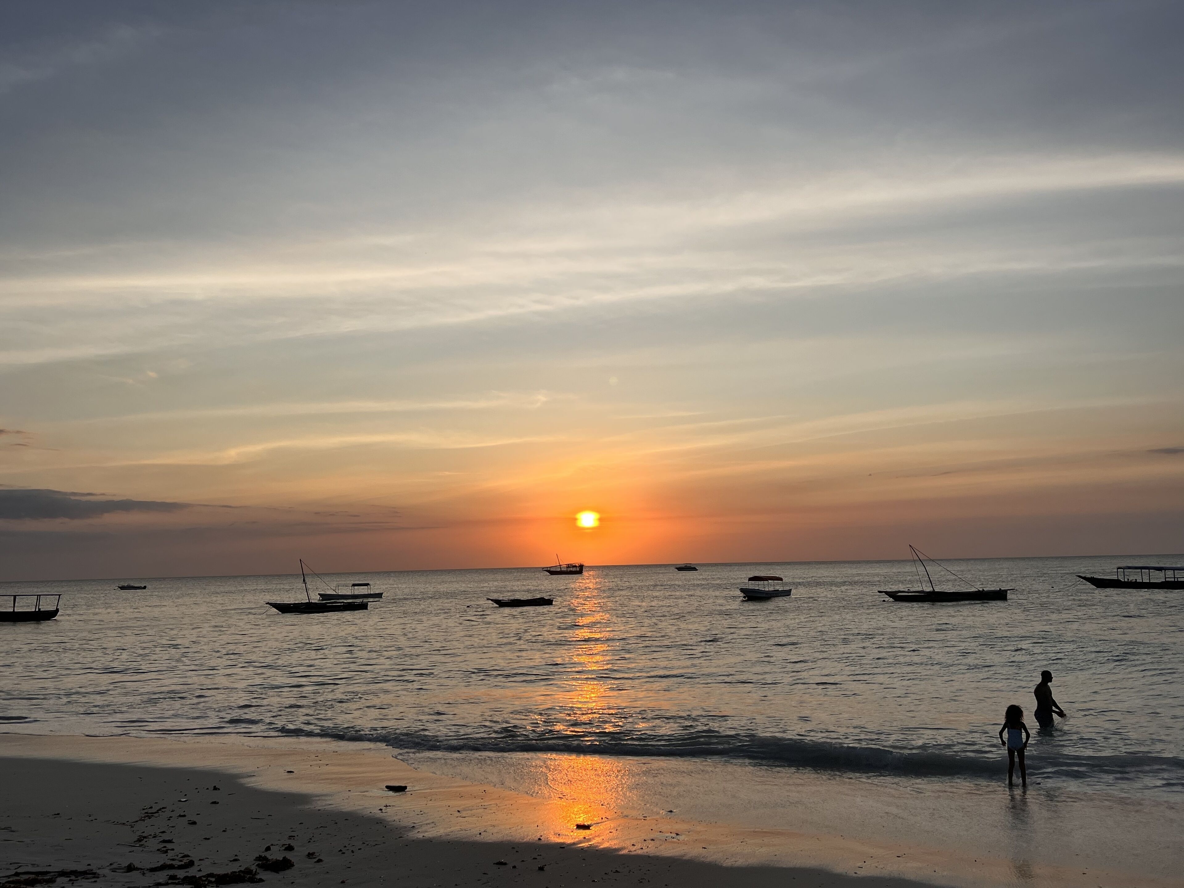 A beach with boats and people near the water during sunset.