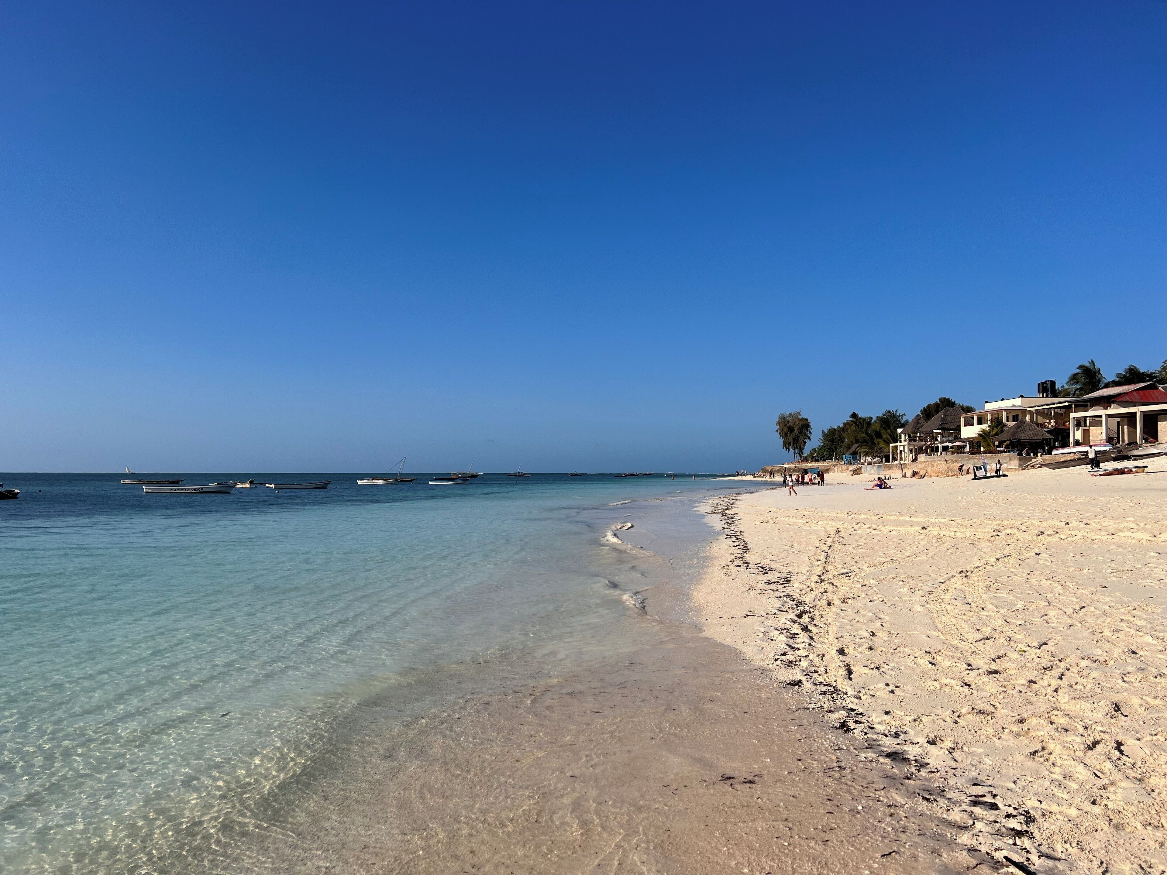 Una playa con aguas cristalinas, barcos y edificios a lo largo de la orilla.