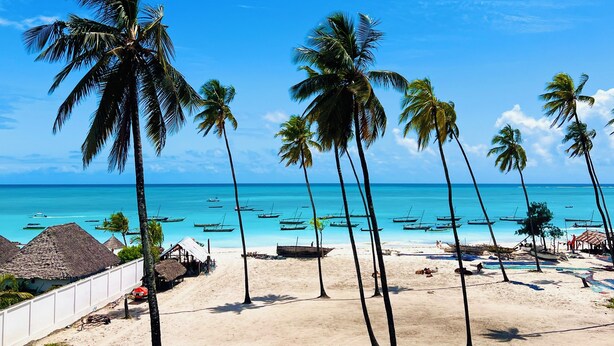 A beach with palm trees, clear blue water, and boats. - Nungwi Beach Front (Nungwi)