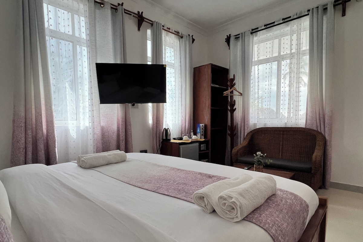 Une chambre d’hôtel comprenant un lit, une télévision, une armoire en bois, une chaise et un bureau avec une bouilloire et des tasses.