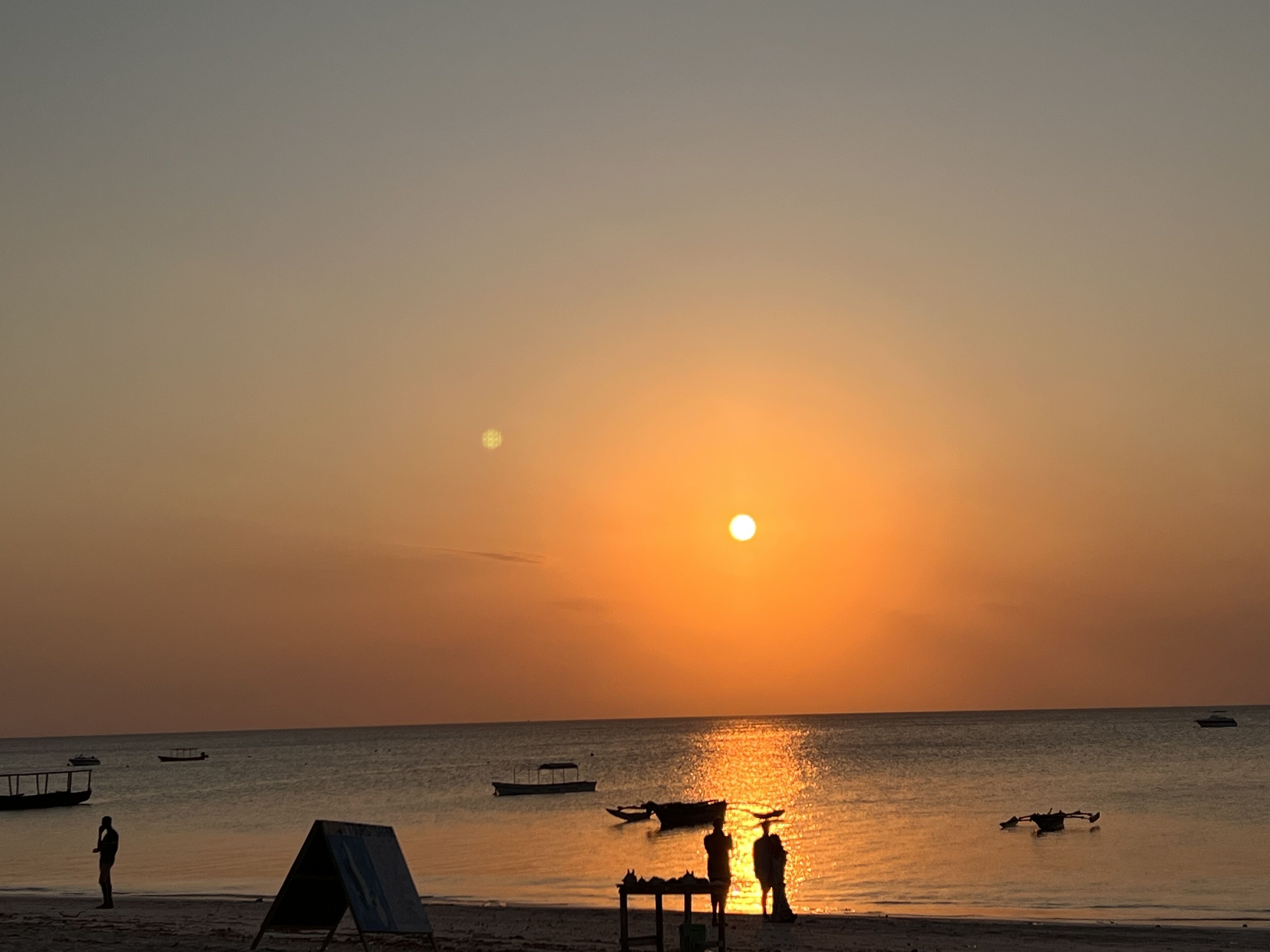 A beach scene with a sunset, boats, and people.