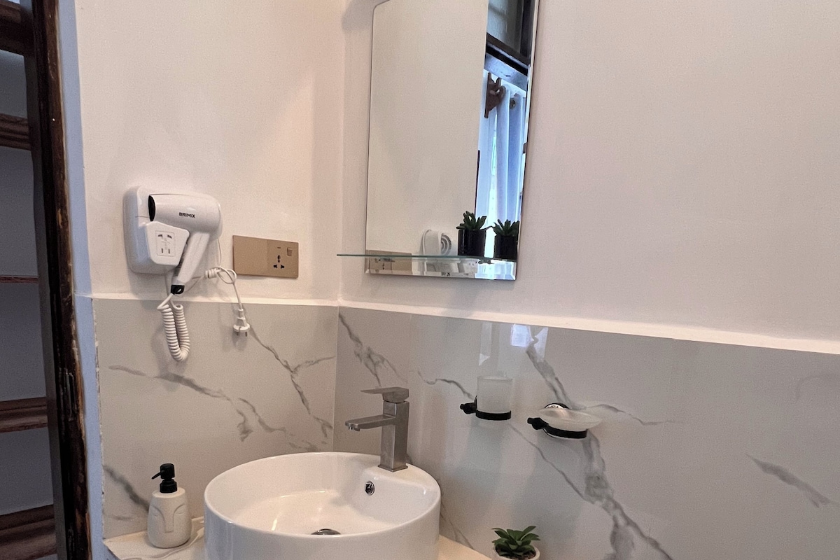 Un bany amb un lavabo blanc, un mirall, un assecador, una barra de tovalloles i un vàter.