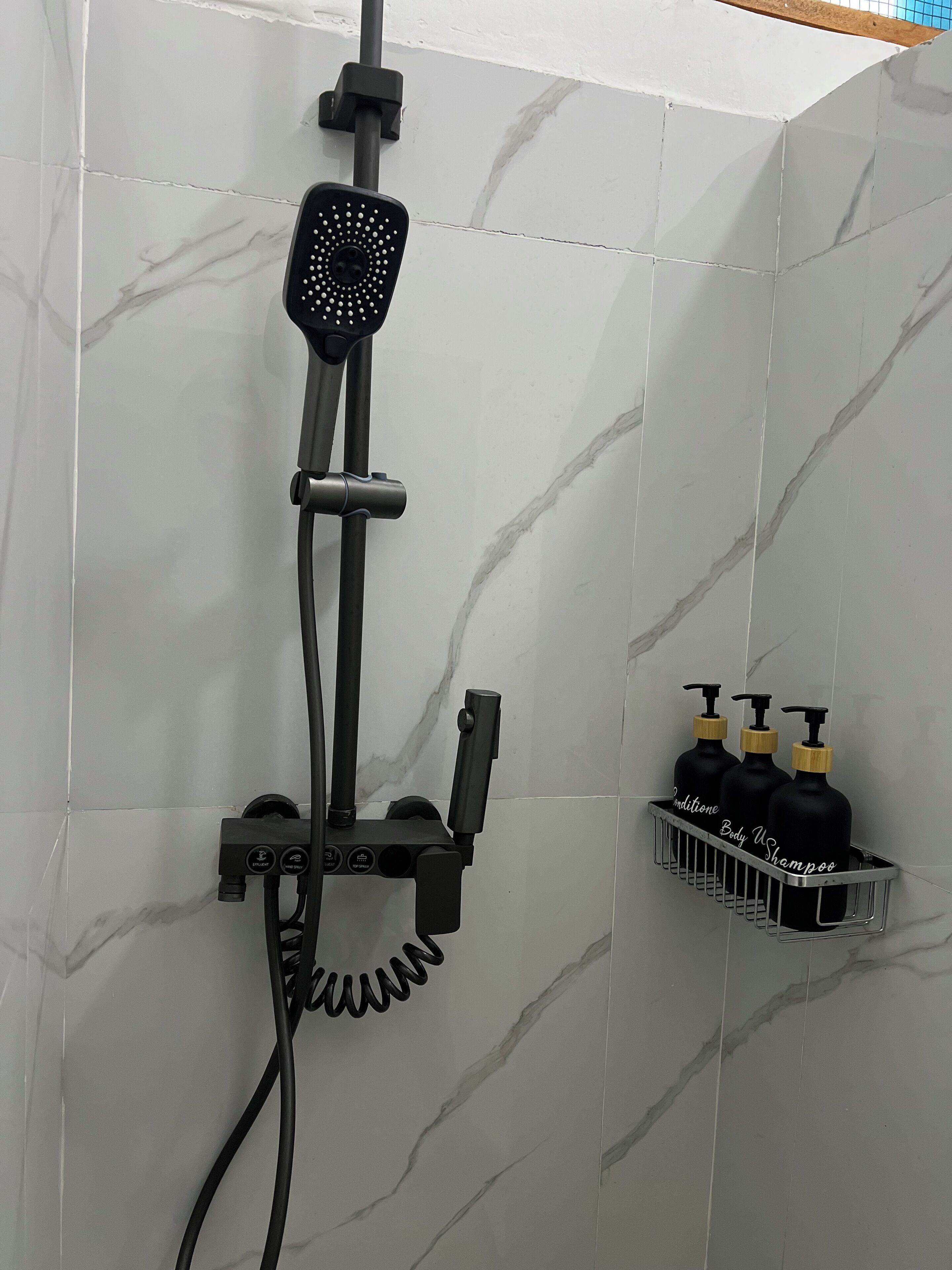 A bathroom with a shower head mounted on a wall, a handheld shower attachment, and a shelf with three bottles of shampoo.