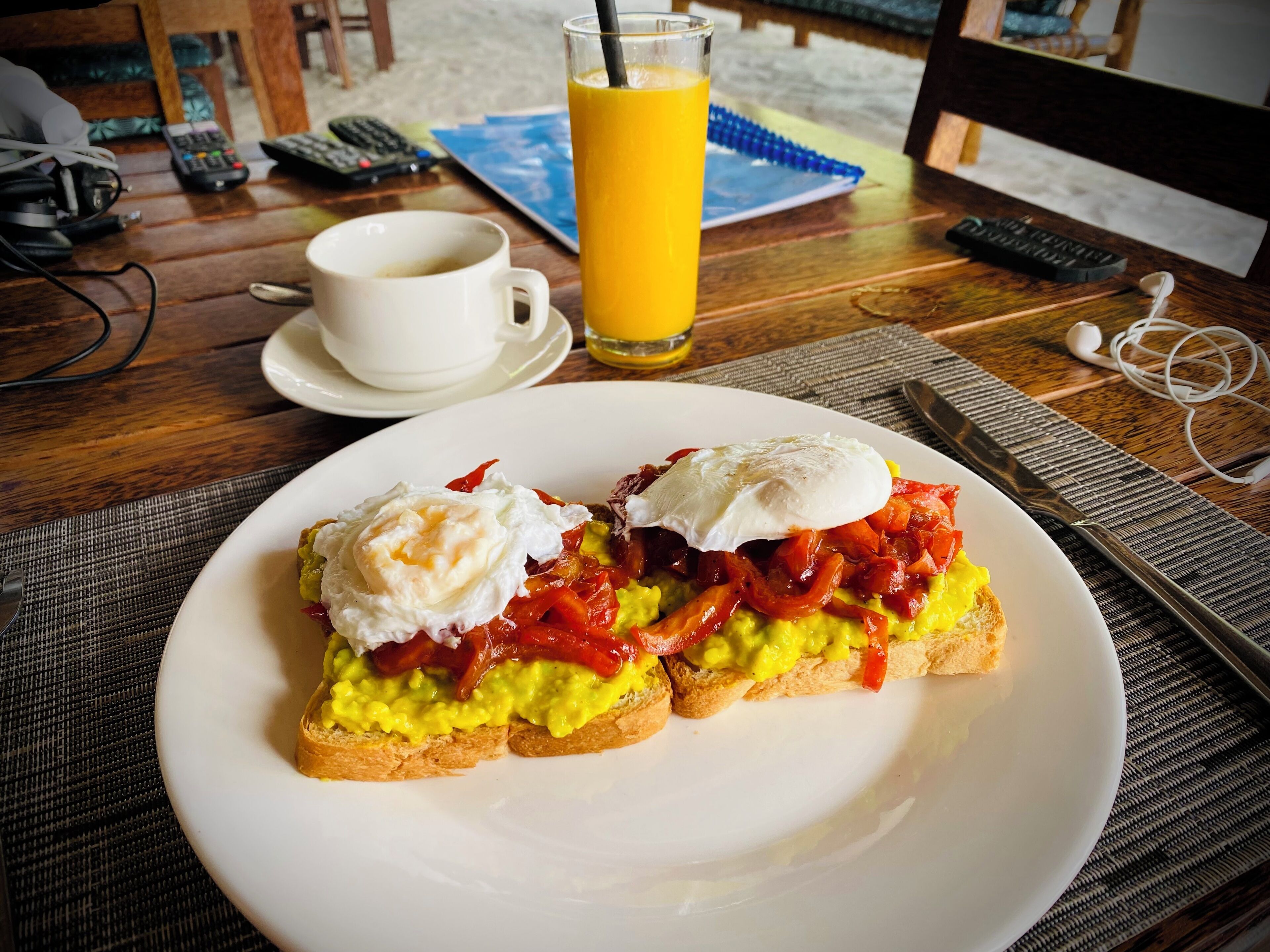 A breakfast plate with eggs, avocado, and red peppers on toast, a glass of orange juice, and a cup of coffee on a wooden table.