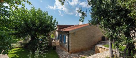 Una pequeña casa de ladrillo con tejado de baldosas, rodeada por un muro de piedra y un camino empedrado.