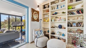 Ein modernes Wohnzimmer mit Sofa, Ohrensessel, Hocker und einer großen, weißen Regaleinrichtung, gefüllt mit Dekoration.
