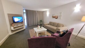 A living room with a TV, sofa, and armchair. There's a plant and a painting on the wall. - Effortless Homes (East London)